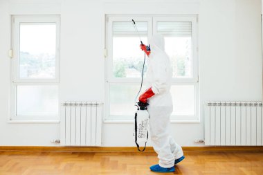 Exterminator in work wear spraying pesticide or insecticide with sprayer  clipart