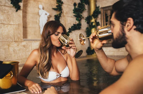 Zevk ve Spa merkezinde rahatlatıcı güzel genç bir çift. Jakuzide oturma ve şarap içme.