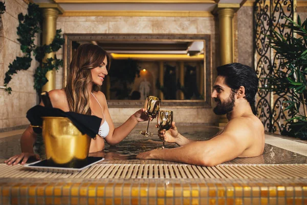 Zevk ve Spa merkezinde rahatlatıcı güzel genç bir çift. Jakuzide oturma ve şarap içme.