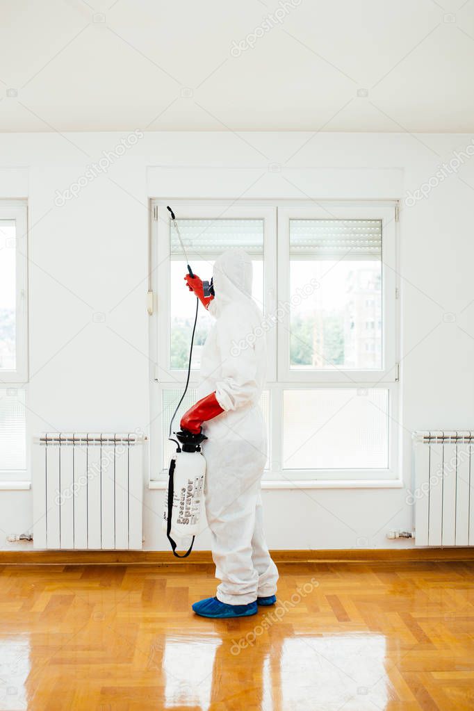 Exterminator in work wear spraying pesticide or insecticide with sprayer 