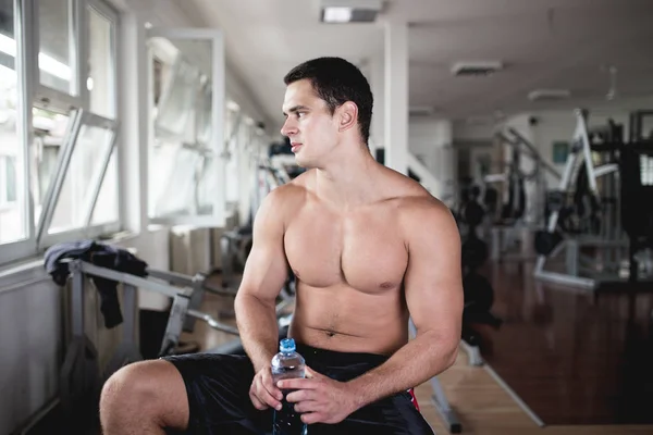 Young attractive adult man drink water at fitness gym. Sport training indoors.