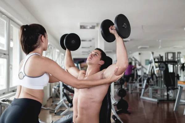 Young attractive adult man and woman exercising and doing weight lifting at fitness gym. Sport training indoors.
