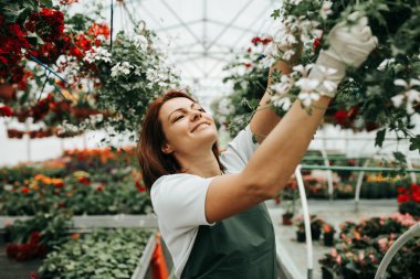 Serada çalışan ve güzel çiçekler zevk Kızıl saçlı genç kadın. Bahçe merkezinde kadın işçisi.