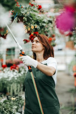 Serada çalışan ve güzel çiçekler zevk Kızıl saçlı genç kadın. Bahçe merkezinde kadın işçisi.