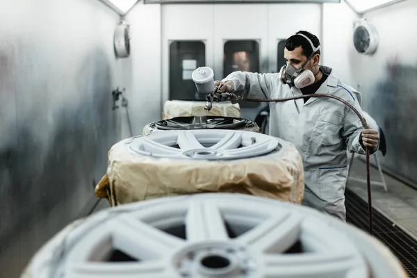 Man with protective clothes and mask painting car parts using spray compressor. Selective focus.