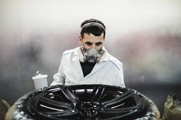Man with protective clothes and mask painting car parts using spray compressor. Selective focus.