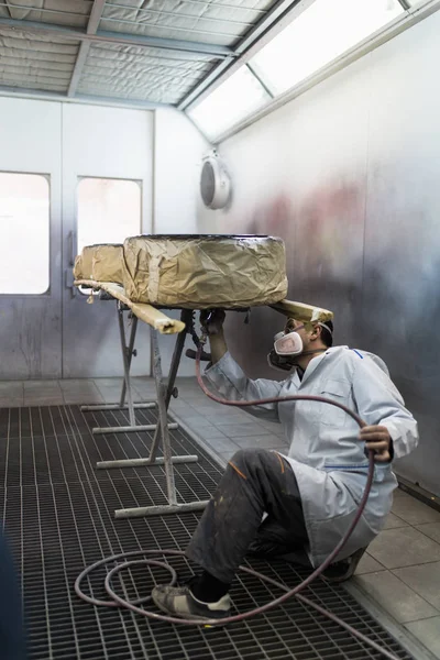 Man with protective clothes and mask painting car parts using spray compressor. Selective focus.