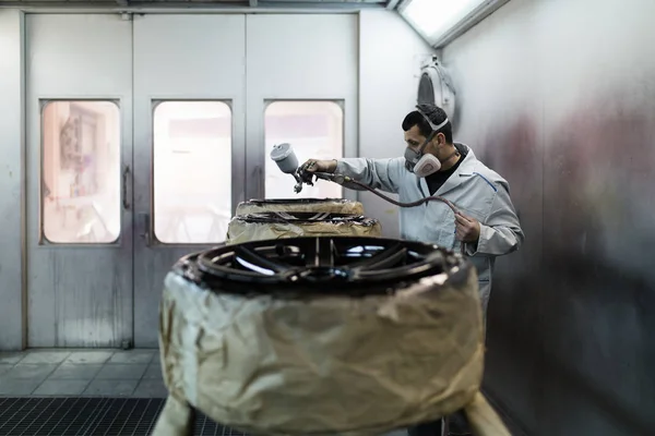 Man with protective clothes and mask painting car parts using spray compressor. Selective focus.