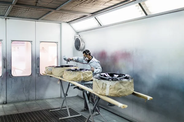 Man with protective clothes and mask painting car parts using spray compressor. Selective focus.