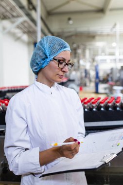 Ciddi orta yaş kadın kalite kontrol işçi şişeleme ve alkolsüz içecek gazlı siyah suyu şişe ambalaj için robot satır denetimi.