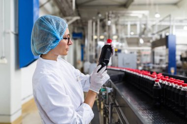 Ciddi orta yaş kadın kalite kontrol işçi şişeleme ve alkolsüz içecek gazlı siyah suyu şişe ambalaj için robot satır denetimi.