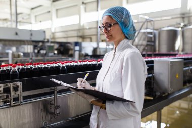 Ciddi orta yaş kadın kalite kontrol işçi şişeleme ve alkolsüz içecek gazlı siyah suyu şişe ambalaj için robot satır denetimi.