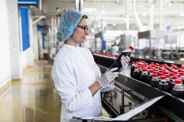 Ciddi orta yaş kadın kalite kontrol işçi şişeleme ve alkolsüz içecek gazlı siyah suyu şişe ambalaj için robot satır denetimi.