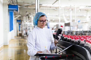 Ciddi orta yaş kadın kalite kontrol işçi şişeleme ve alkolsüz içecek gazlı siyah suyu şişe ambalaj için robot satır denetimi.