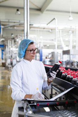Ciddi orta yaş kadın kalite kontrol işçi şişeleme ve alkolsüz içecek gazlı siyah suyu şişe ambalaj için robot satır denetimi.