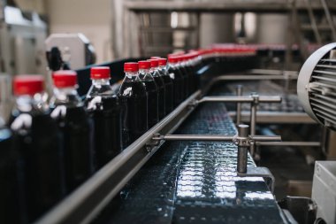 Şişeleme fabrikası - siyah meyve suyu veya meşrubat işleme ve şişe suyu şişeleme için satır şişeleme. Seçici odak. 