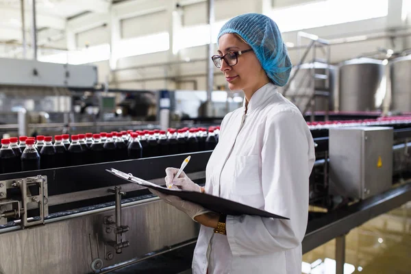 Ciddi orta yaş kadın kalite kontrol işçi şişeleme ve alkolsüz içecek gazlı siyah suyu şişe ambalaj için robot satır denetimi.