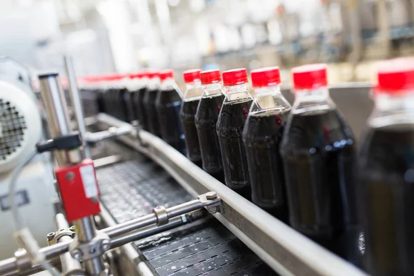 Bottling factory - Black juice or soft drink bottling line for processing and bottling juice into bottles. Selective focus.