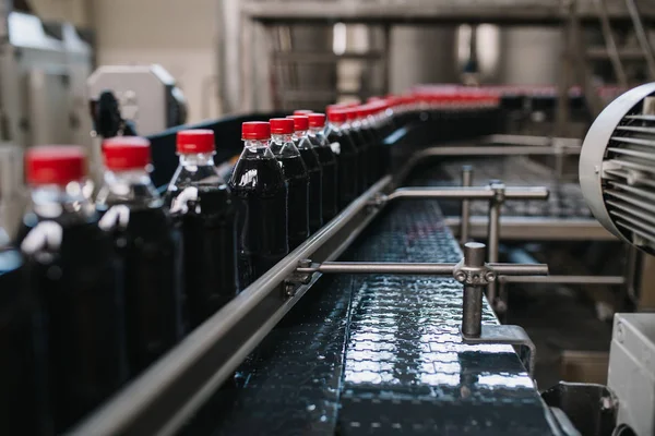 Bottling factory - Black juice or soft drink bottling line for processing and bottling juice into bottles. Selective focus.