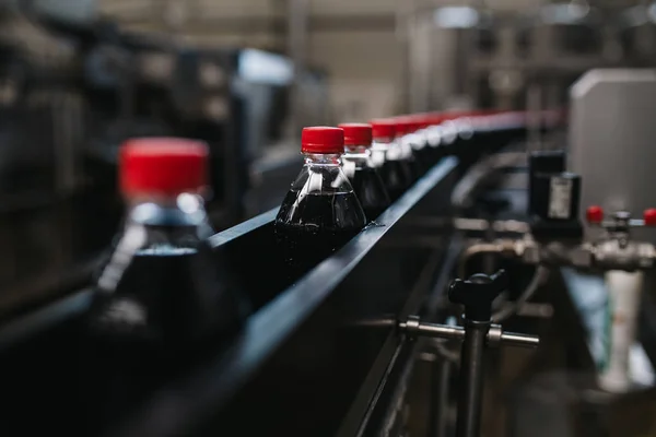 Bottling factory - Black juice or soft drink bottling line for processing and bottling juice into bottles. Selective focus.