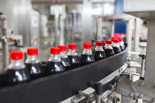 Bottling factory - Black juice or soft drink bottling line for processing and bottling juice into bottles. Selective focus.