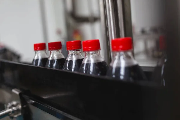 Bottling factory - Black juice or soft drink bottling line for processing and bottling juice into bottles. Selective focus.