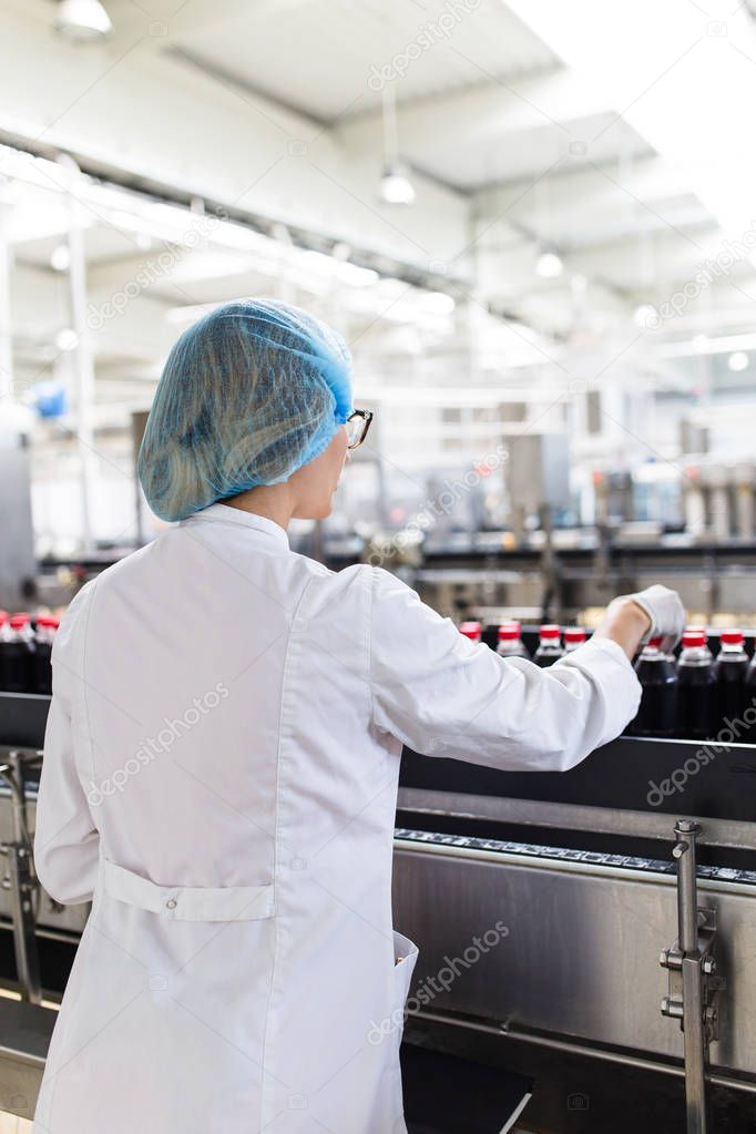 Serious middle age woman quality control worker checking robotic line for bottling and packaging carbonated black juice of soft drink into bottles.