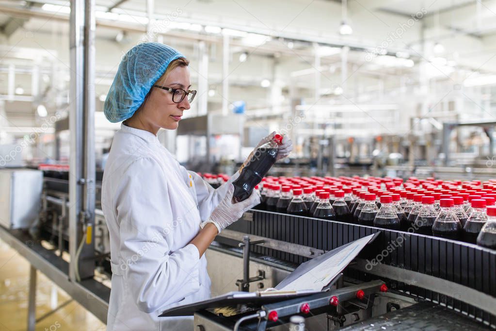 Serious middle age woman quality control worker checking robotic line for bottling and packaging carbonated black juice of soft drink into bottles.