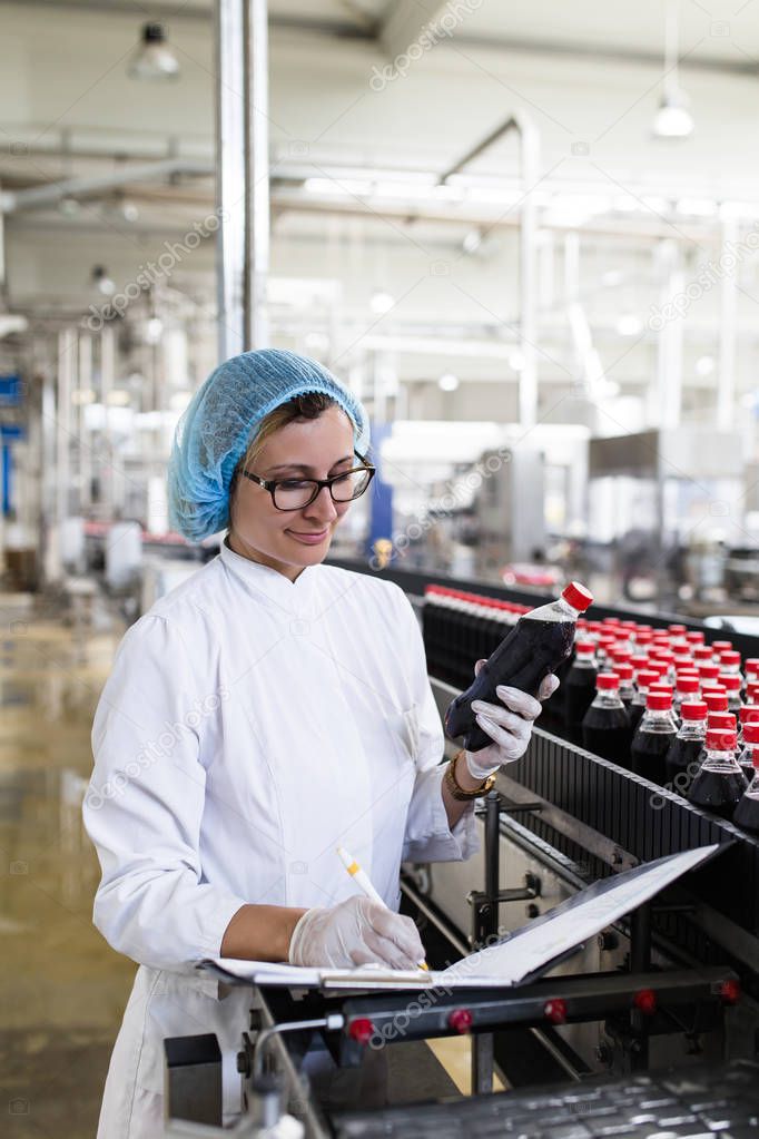 Serious middle age woman quality control worker checking robotic line for bottling and packaging carbonated black juice of soft drink into bottles.