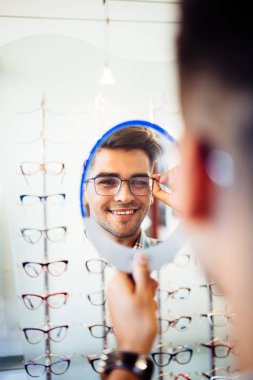 Yakışıklı genç adam gözlük çerçevesini optik mağazada seçiyor..