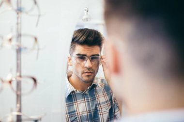 Yakışıklı genç adam gözlük çerçevesini optik mağazada seçiyor..