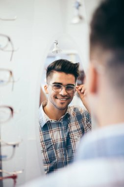 Yakışıklı genç adam gözlük çerçevesini optik mağazada seçiyor..