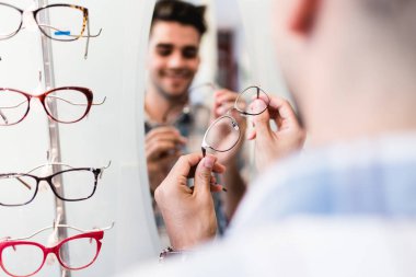 Yakışıklı genç adam gözlük çerçevesini optik mağazada seçiyor..