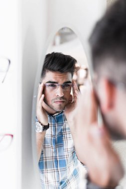 Yakışıklı genç adam gözlük çerçevesini optik mağazada seçiyor..