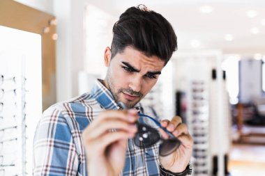 Yakışıklı genç adam gözlük çerçevesini optik mağazada seçiyor..