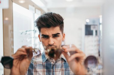 Yakışıklı genç adam gözlük çerçevesini optik mağazada seçiyor..