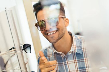 Yakışıklı genç adam gözlük çerçevesini optik mağazada seçiyor..