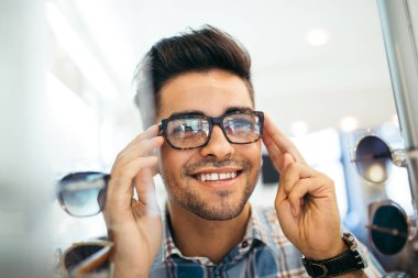Yakışıklı genç adam gözlük çerçevesini optik mağazada seçiyor..