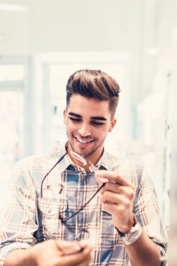 Yakışıklı genç adam gözlük çerçevesini optik mağazada seçiyor..