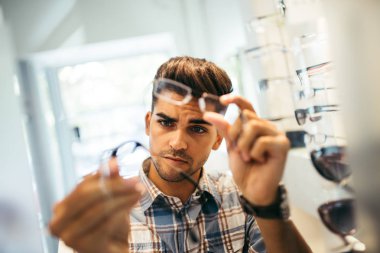 Yakışıklı genç adam gözlük çerçevesini optik mağazada seçiyor..