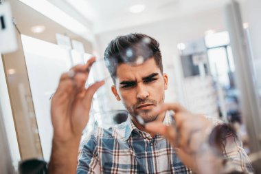 Yakışıklı genç adam gözlük çerçevesini optik mağazada seçiyor..