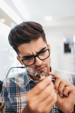 Yakışıklı genç adam gözlük çerçevesini optik mağazada seçiyor..