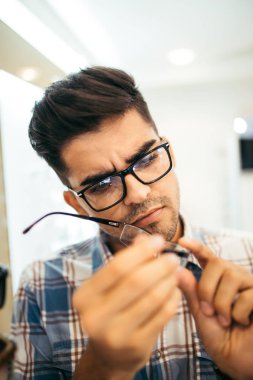 Yakışıklı genç adam gözlük çerçevesini optik mağazada seçiyor..