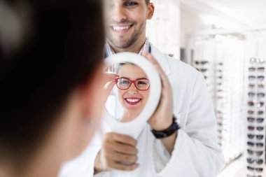 Genç optometrist müşteriye sağ gözlük seçmesinde yardımcı olur