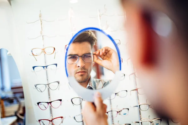 Yakışıklı Genç Adam Gözlük Çerçevesini Optik Mağazada Seçiyor — Stok fotoğraf