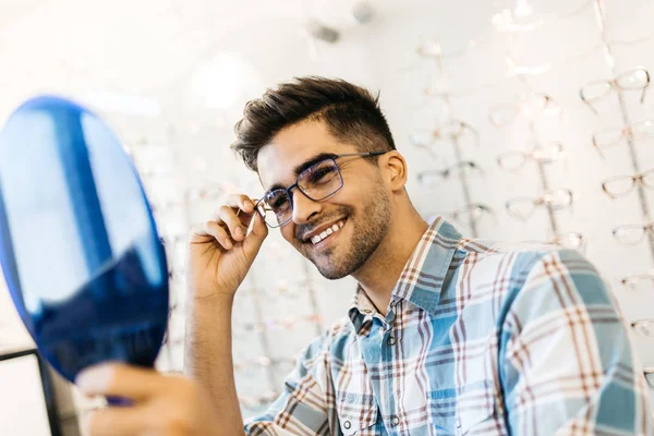 Yakışıklı genç adam gözlük çerçevesini optik mağazada seçiyor..