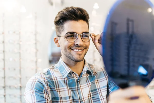 Yakışıklı genç adam gözlük çerçevesini optik mağazada seçiyor..