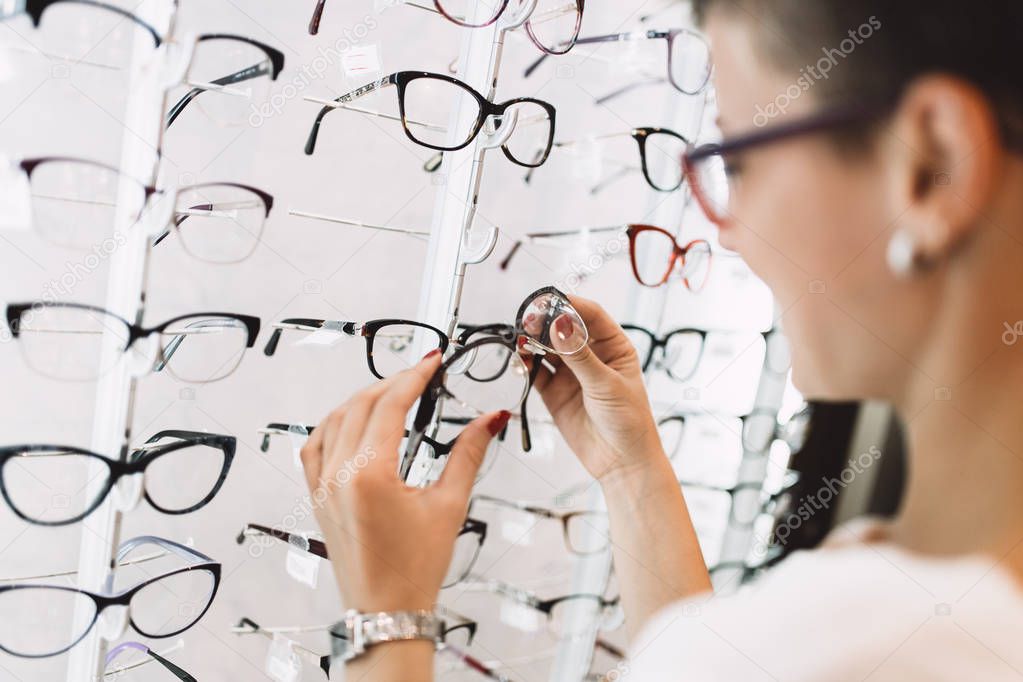 Beautiful middle age woman choosing a glasses in optician store.