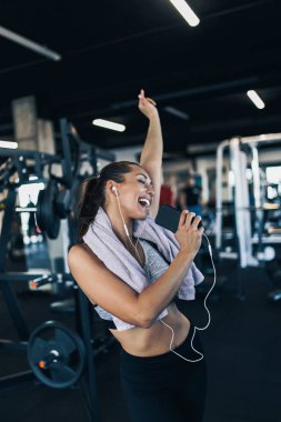 Modern fitness spor salonu dans, gülümseyen ve şarkı başarılı egzersiz sonra genç çekici kadın. O kablolu kulaklıklar ve bakış telefon ile müzik dinlerken.