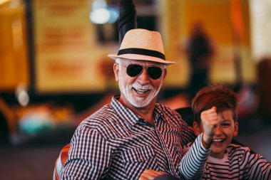 Büyükbaba ve torunu eğlenmek ve eğlence parkında birlikte iyi kaliteli zaman harcamak. Onlar zevk ve birlikte tampon araba sürerken gülümseyen.